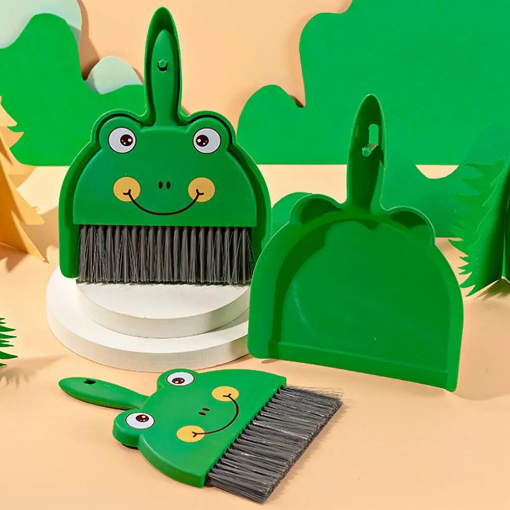 Green dinosaur-shaped broom and dustpan set on a beige background with green leaves.