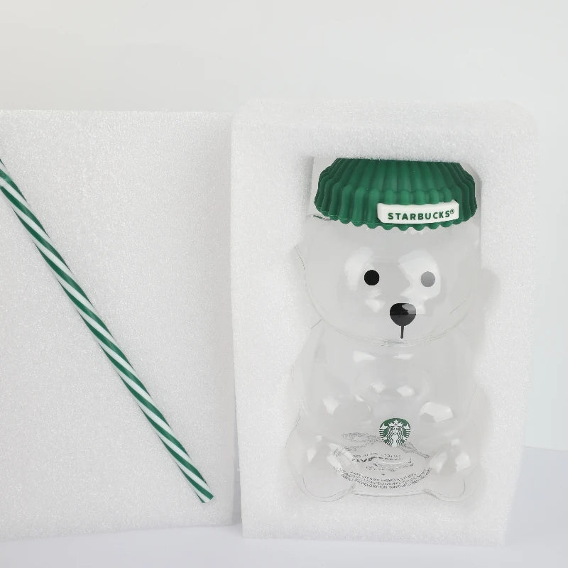 Starbucks Bearista Bear glass tumbler with green lid next to a striped straw and packaging foam