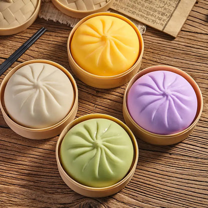 Four steamed buns in round bamboo steamers arranged on a wooden table. The buns are in four colors: white, yellow, light green, and light purple.