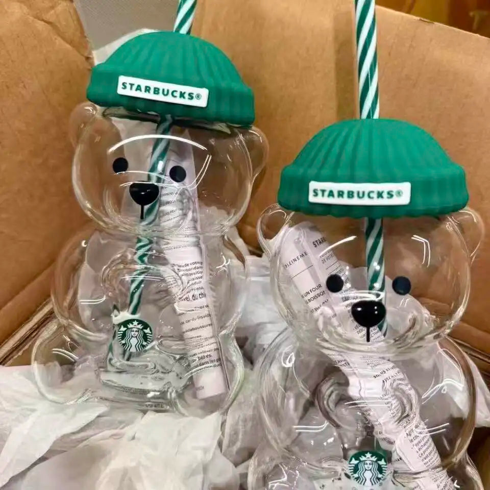 Two bear-shaped Starbucks cups with green lids and straws on a cardboard surface.