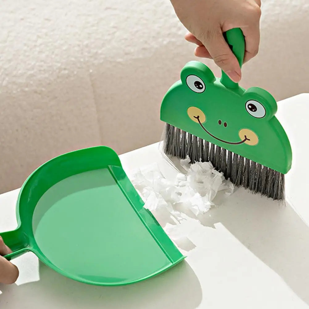 Green children's dustpan and brush set with a frog design on a white surface.