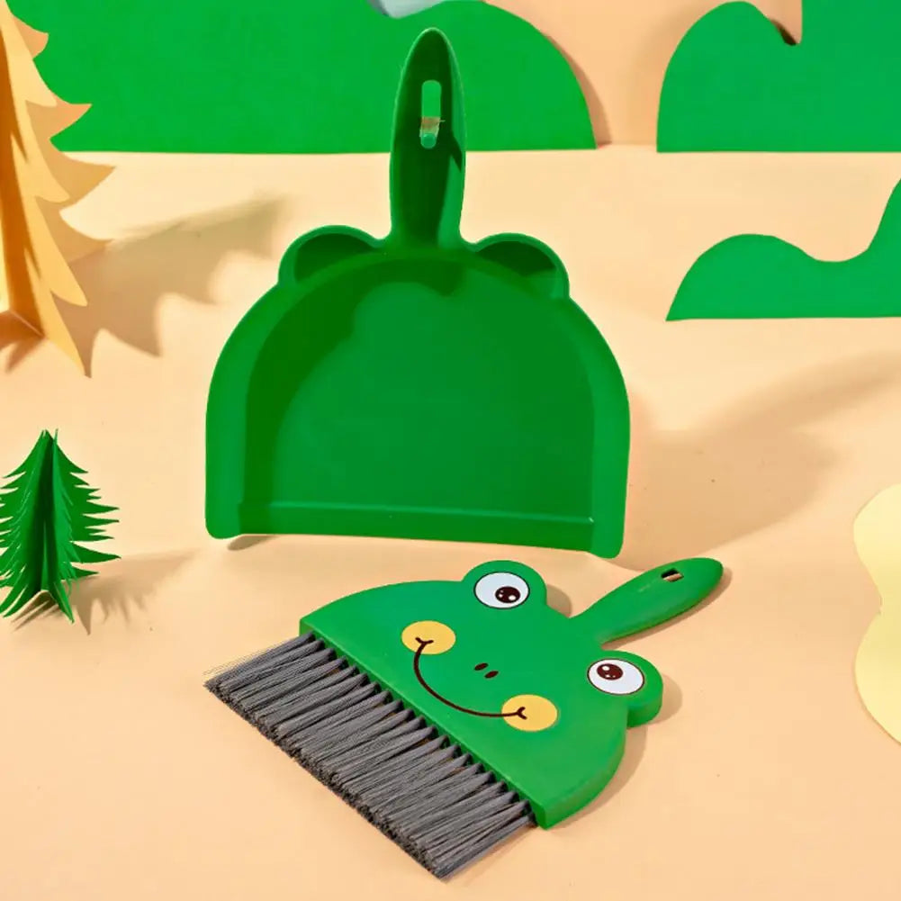 Green frog-shaped broom and dustpan set on a beige background with green tree decorations.
