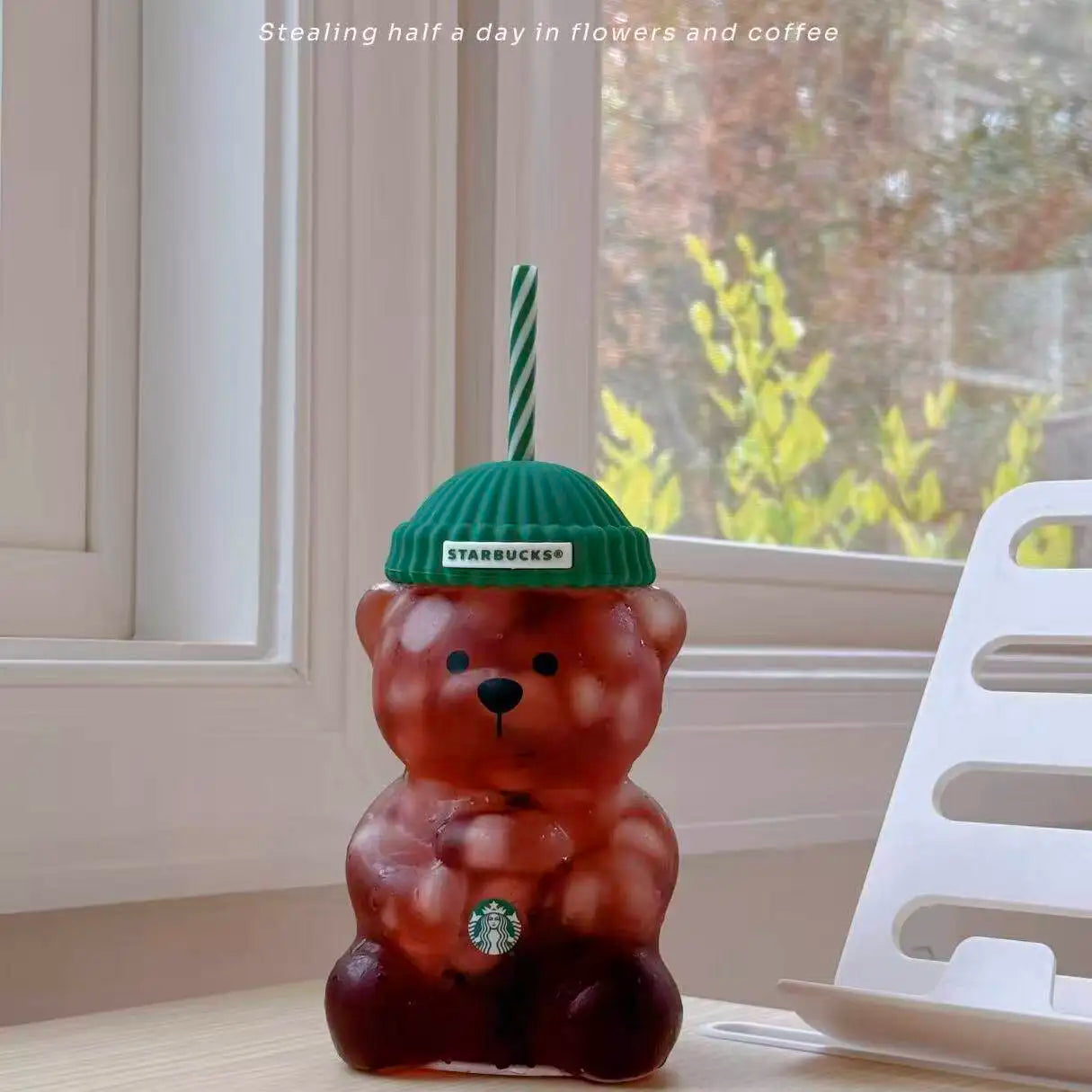 Red-toned Starbucks Bearista Bear tumbler with green lid and straw on a windowsill