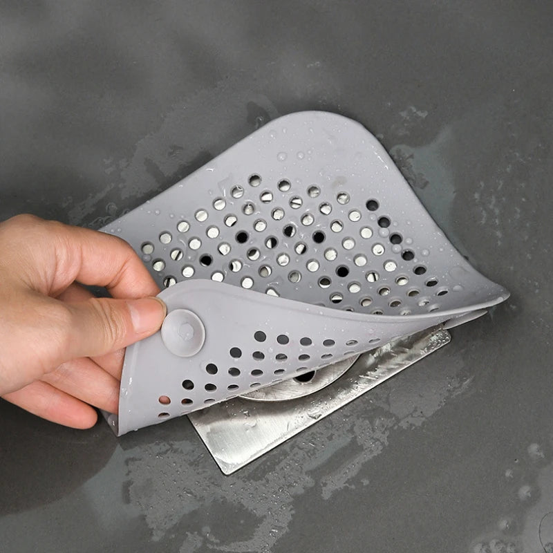 Gray silicone strainer held by a hand over a sink.