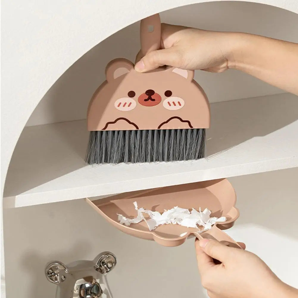 Cute bear-shaped dustpan and brush set with a person using it to collect debris.